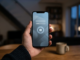 En hand håller en smartphone med en pausikon på skärmen i ett svagt upplyst rum, som symbol för självavstängning från spel.